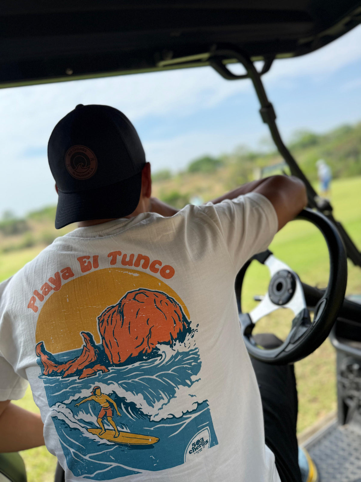 Person wearing the Playa El Tunco graphic T-shirt while driving a golf cart